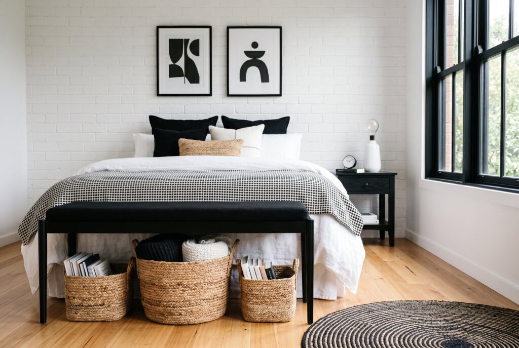 Woven rattan baskets under black bed frame in modern black and white bedroom. 