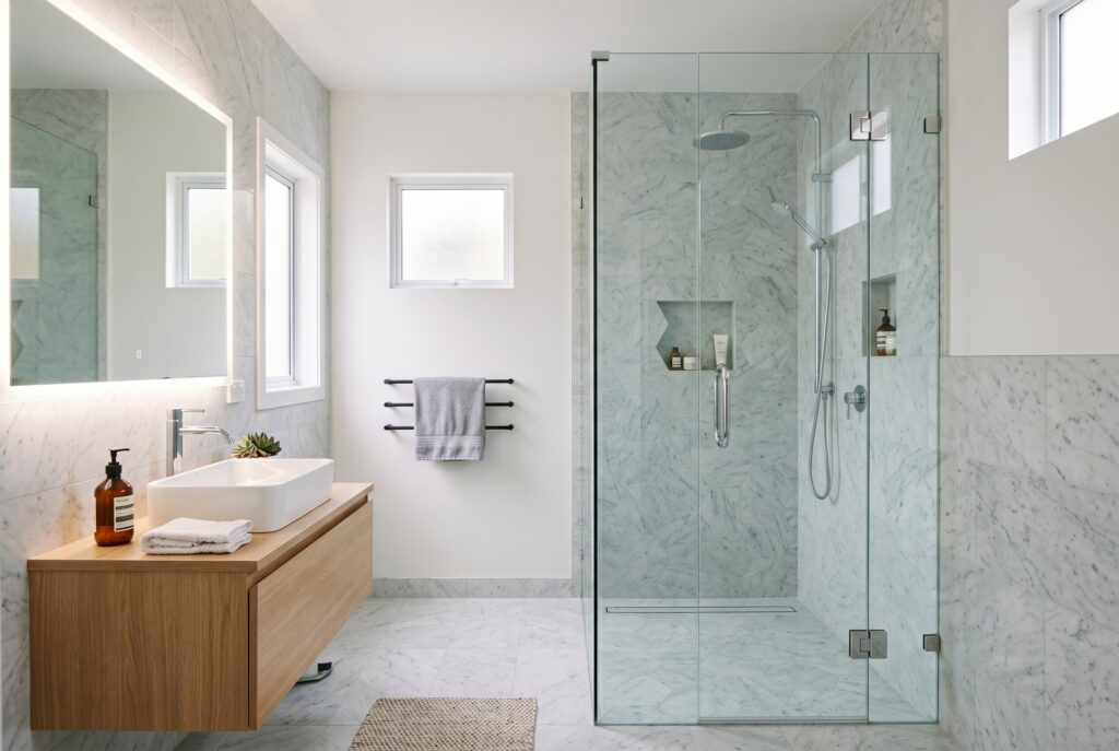 Frameless glass walk in shower with floating wood vanity and modern bathroom layout. 