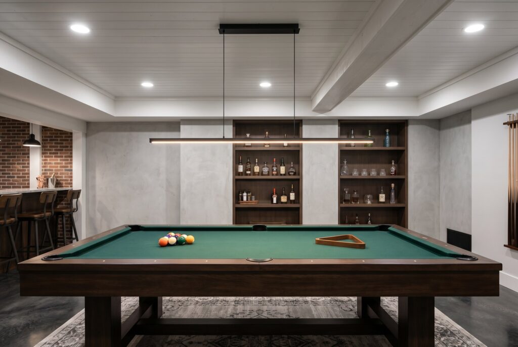 Slim linear pendant light suspended above basement pool table and entertainment zone.