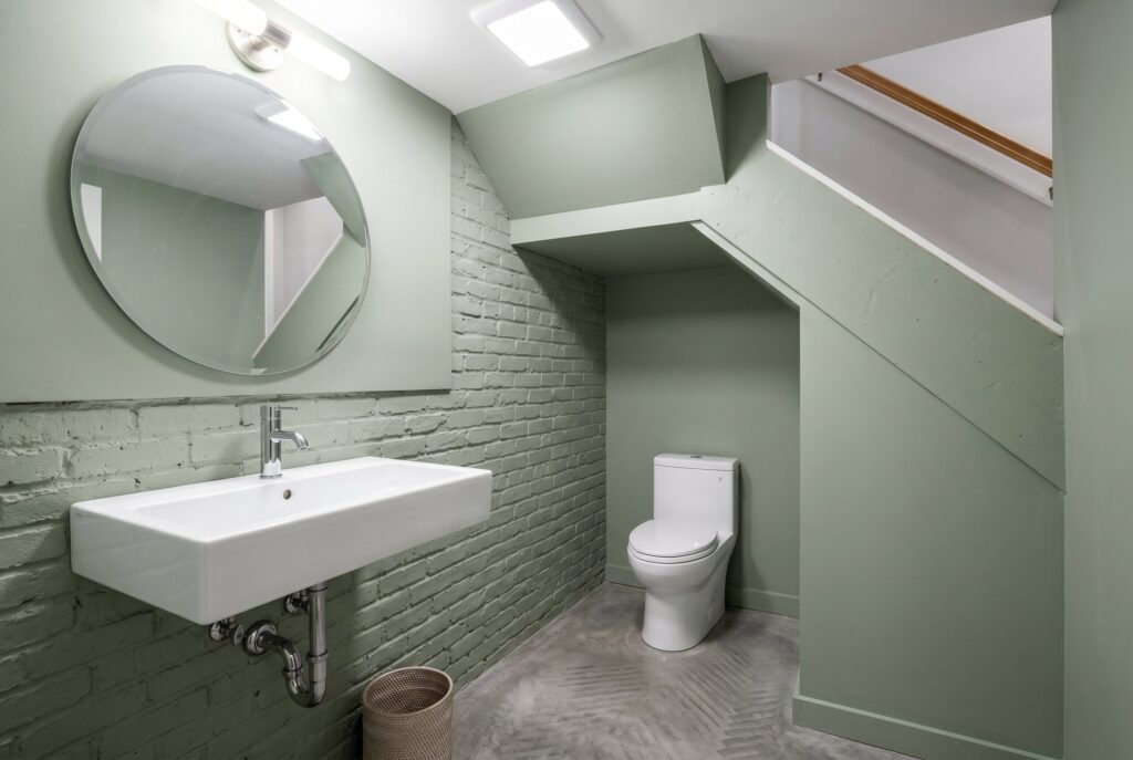 Under stair powder room with wall mounted sink, sage green walls, and round mirror.