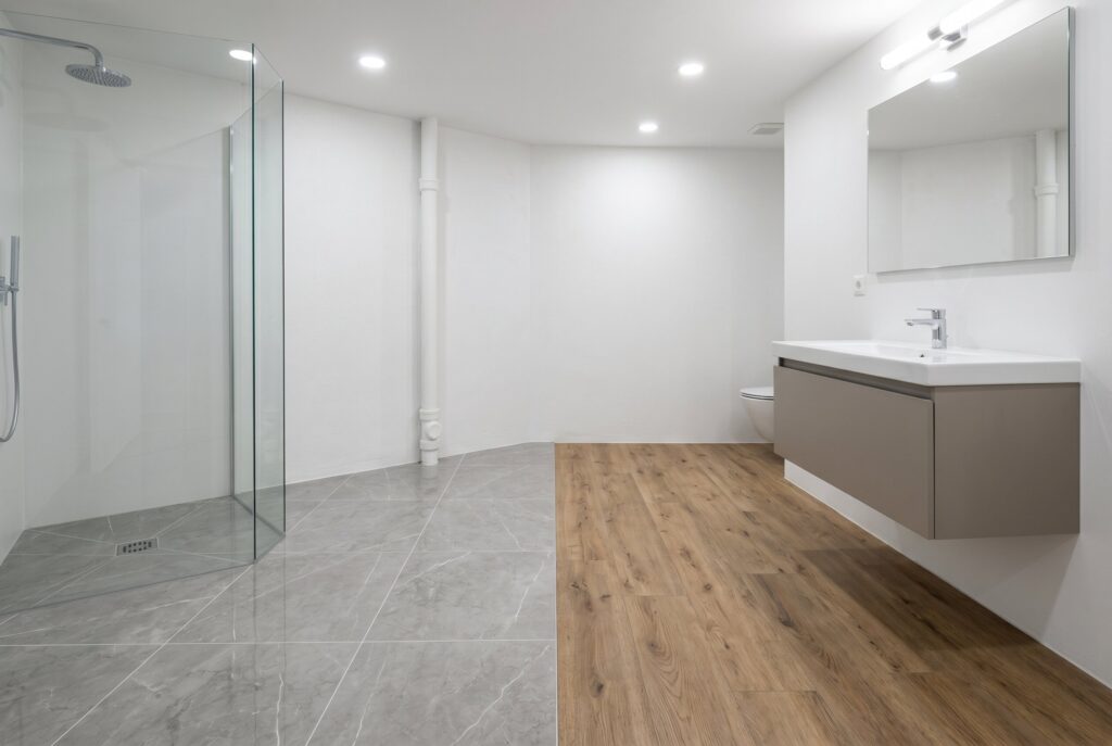Waterproof basement bathroom flooring with porcelain tile shower zone and LVP flooring.