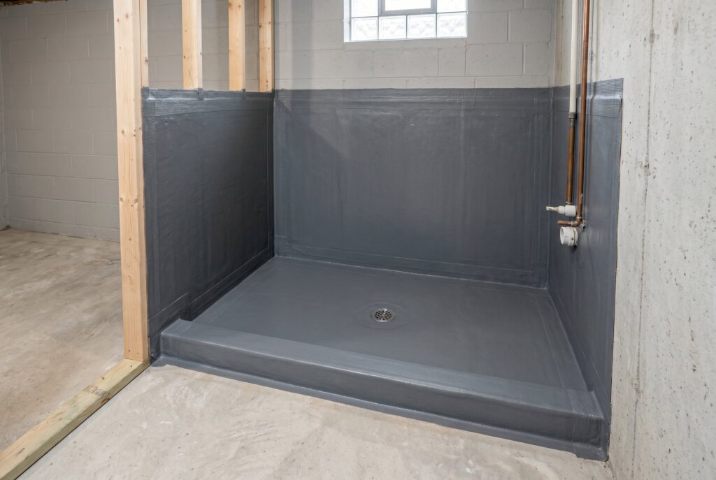 Waterproof shower pan system installed before tile work in basement bathroom construction.