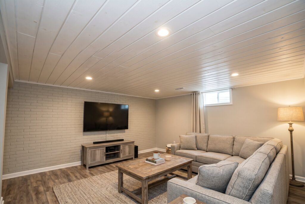 White shiplap basement ceiling above sectional seating and media wall.