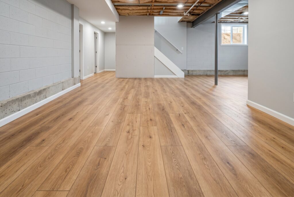 Wide plank laminate flooring in unfinished basement with exposed ceiling and open floor plan.
