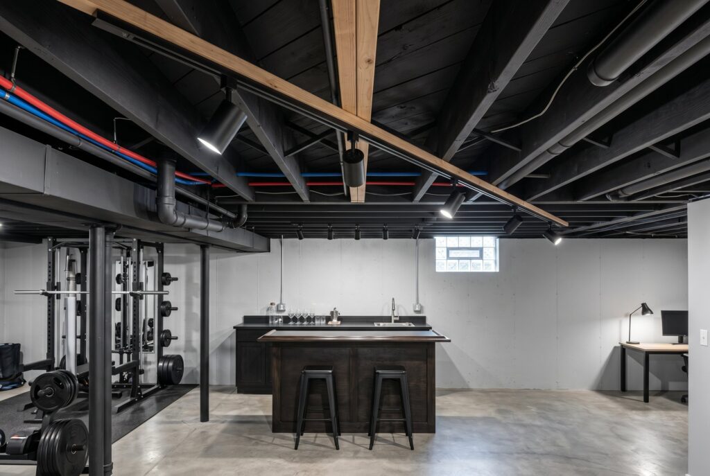 Track lighting mounted on black exposed basement ceiling above gym and game area.