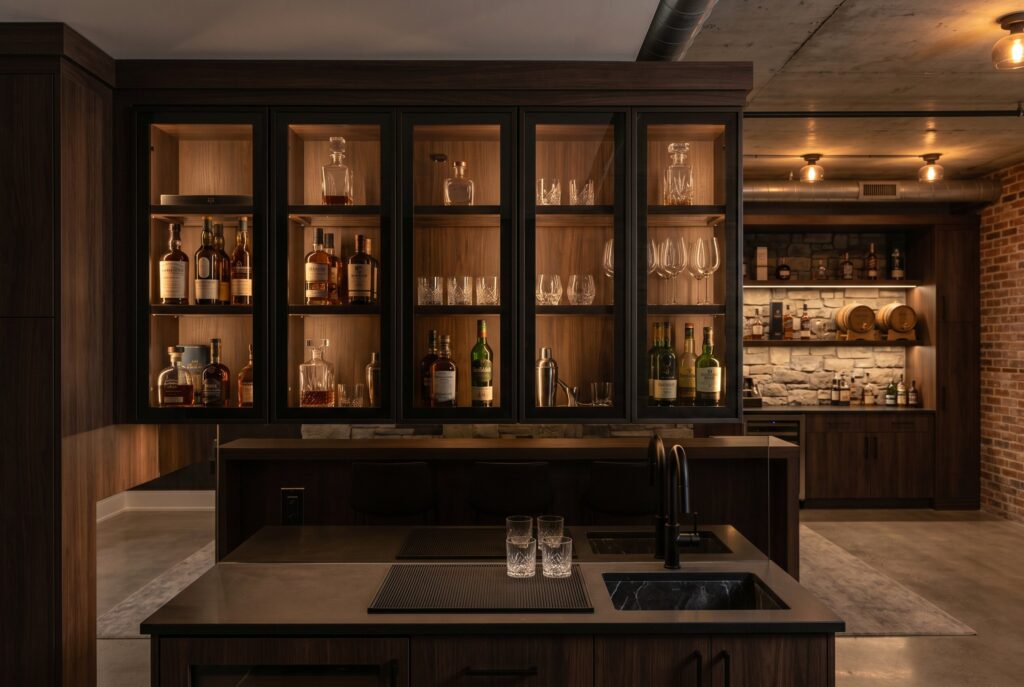 Moody basement bar with smoked glass cabinets and warm illuminated shelving. 