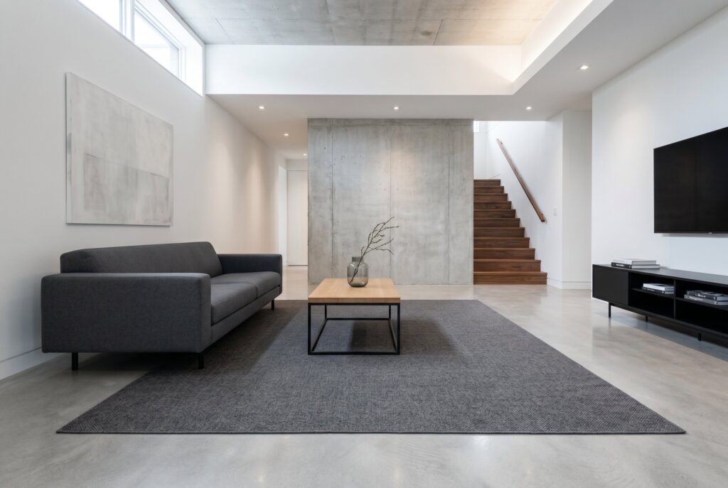 Minimalist modern basement lounge with polished surfaces, oversized rug, and clean lines.