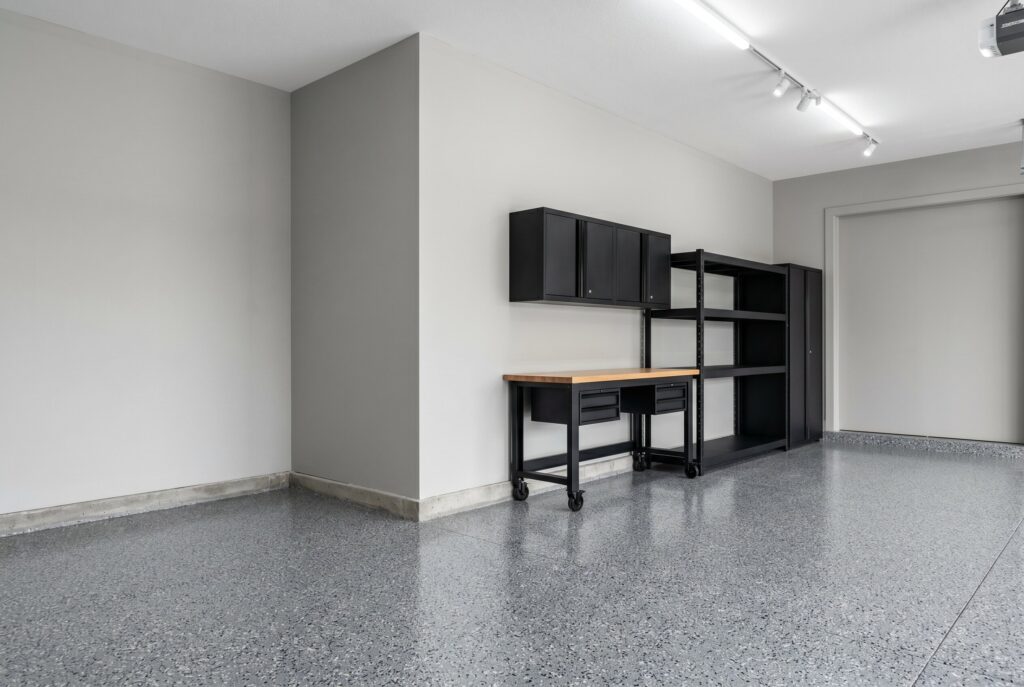A garage painted in Sherwin Williams Repose Gray, a classic cool gray, featuring bright LED track lighting, black storage cabinets, and a gray flake epoxy floor.