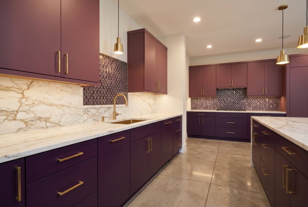 Aubergine and plum kitchen cabinets with brass accents, marble countertops, and bold expressive palette. 