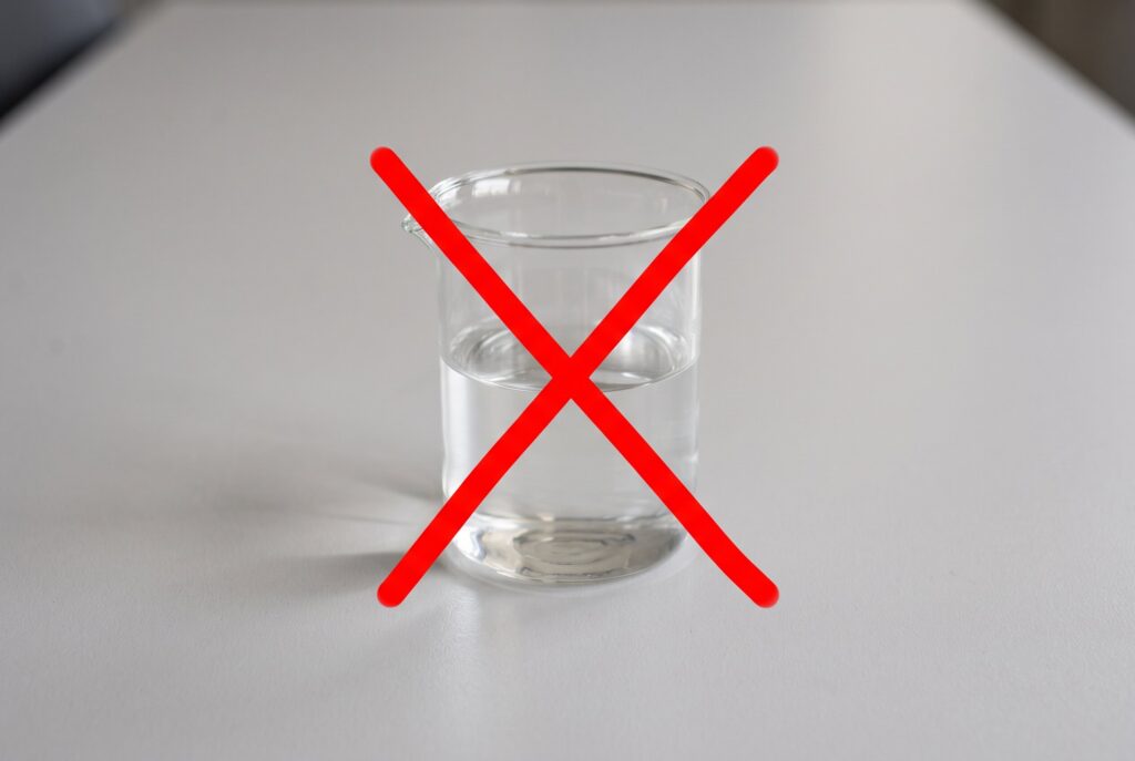 A glass filled with liquid and marked with a large red X to emphasize that mixing vinegar and bleach is dangerous.