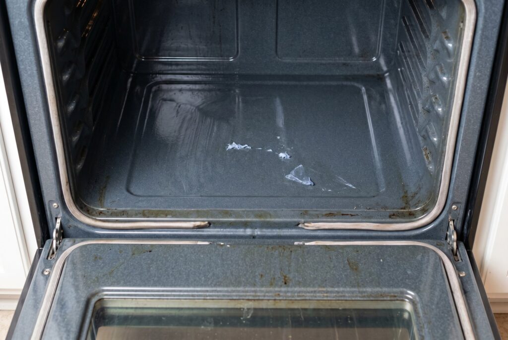 An empty oven interior showing loose food residue on the bottom before the self-cleaning cycle begins.