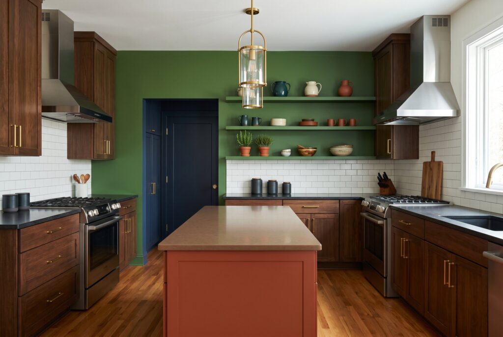 Color drenched kitchen with deep green walls, aubergine pantry, walnut cabinetry, and warm island.