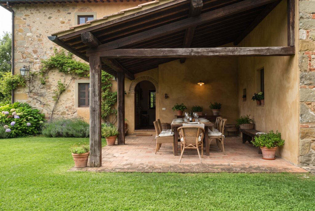 Shaded loggia with a sloped wooden roof, timber posts, terracotta-paved dining area, and adjacent green lawn.