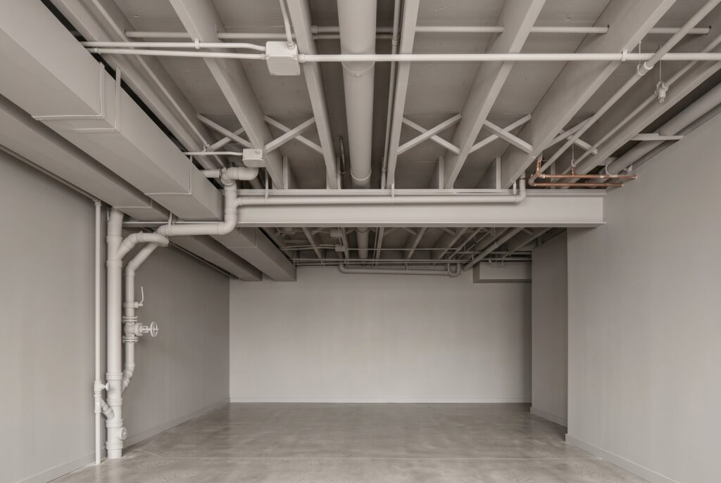 Color drenched basement ceiling with exposed pipes painted in matching neutral tone.