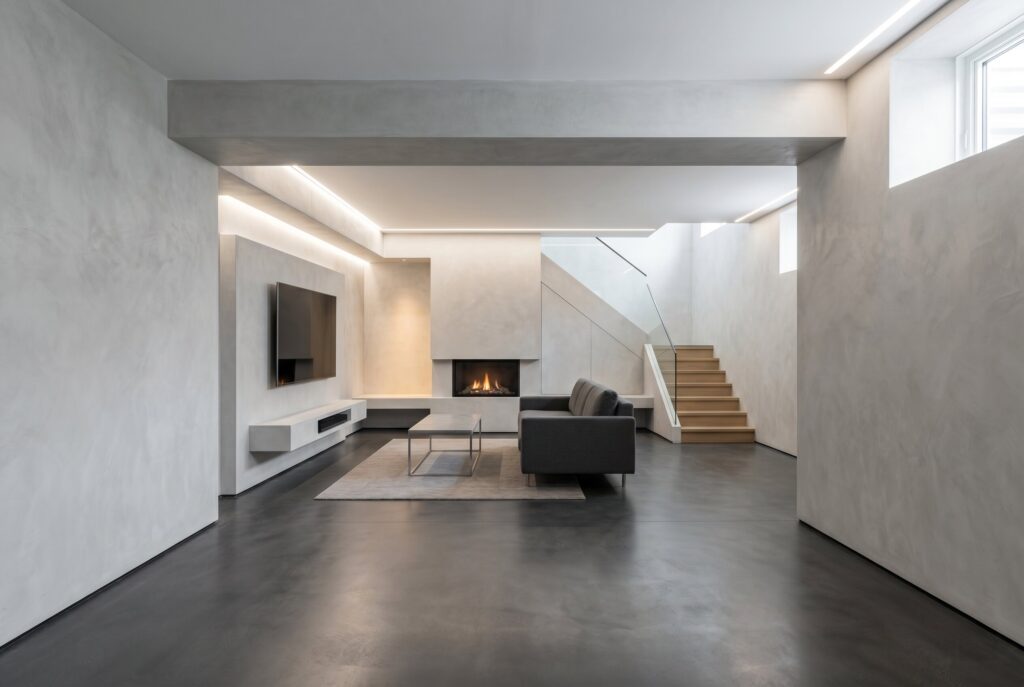 Seamless micro cement walls in minimalist basement with fireplace and floating cabinetry.