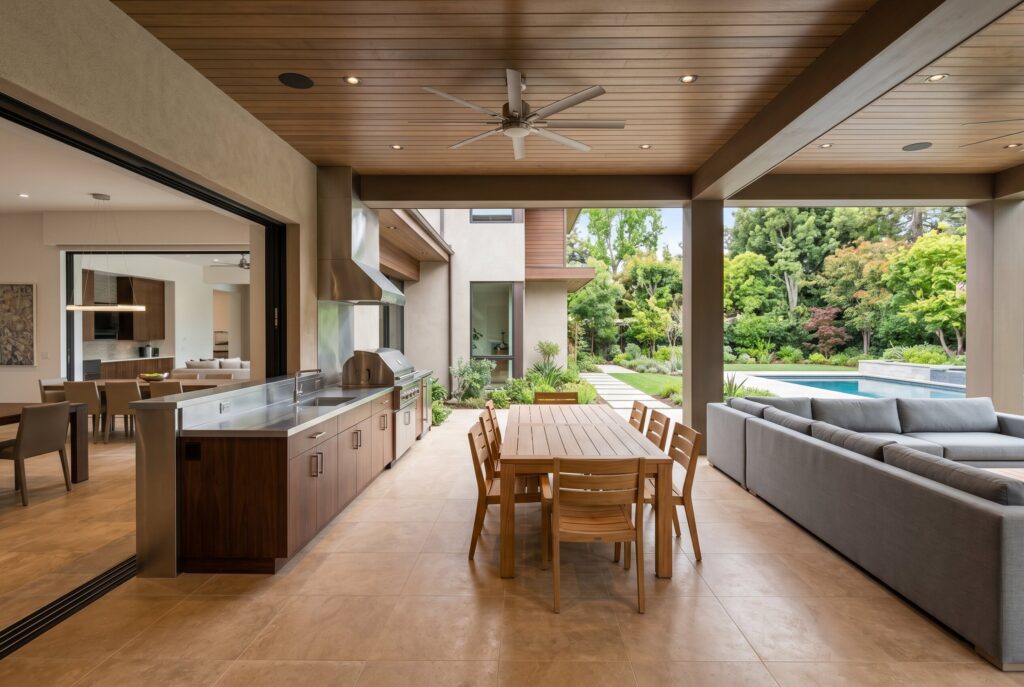 All season screened outdoor kitchen with dark cabinetry, stone counters, and ceiling fan. 