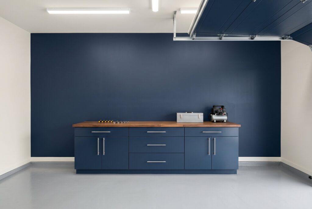 A garage featuring a Benjamin Moore Hale Navy feature wall paired with blue lower cabinets, a wood countertop, and a light gray epoxy floor.
