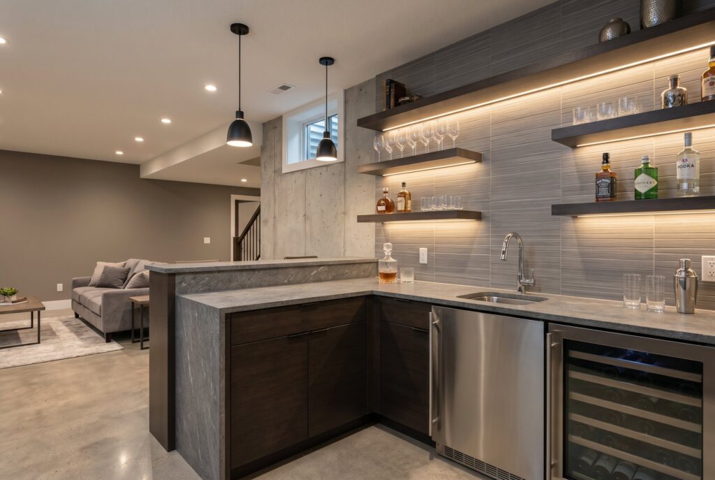 Modern wet bar with stone countertop, beverage fridge, and floating illuminated shelves.