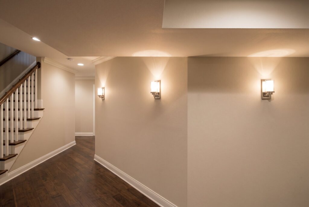 Uplighting wall sconces casting light upward along basement hallway walls.