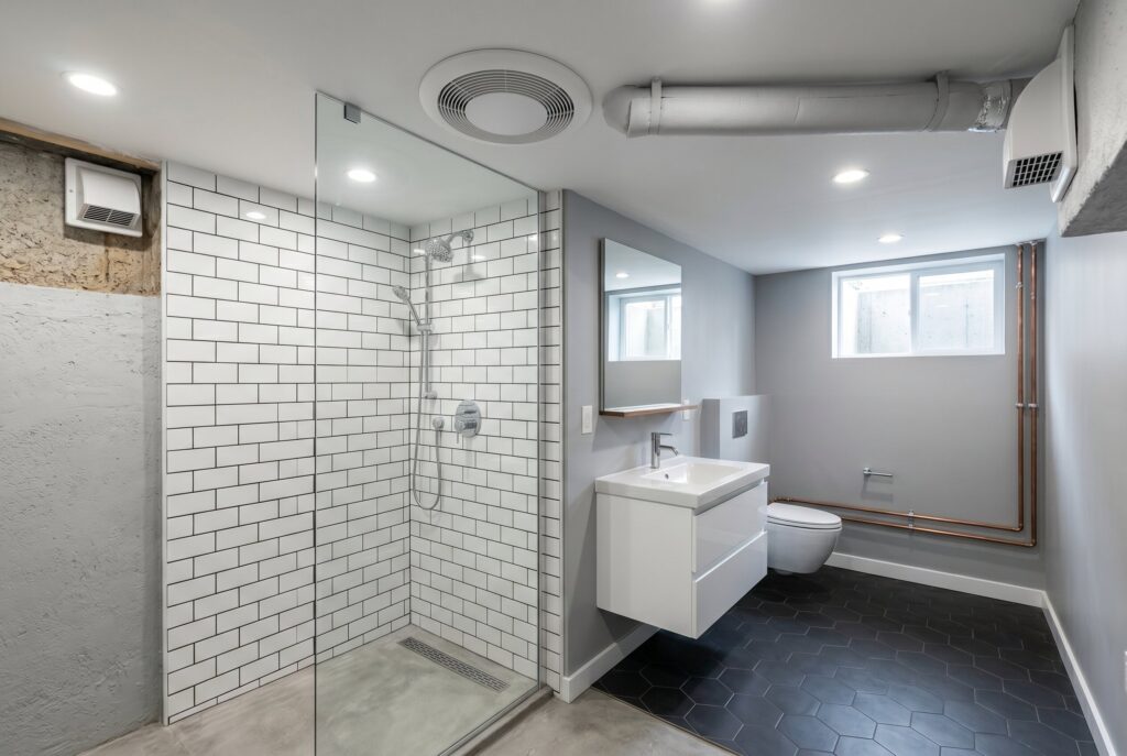 Basement bathroom with glass shower, floating vanity, and ceiling mounted ventilation system.