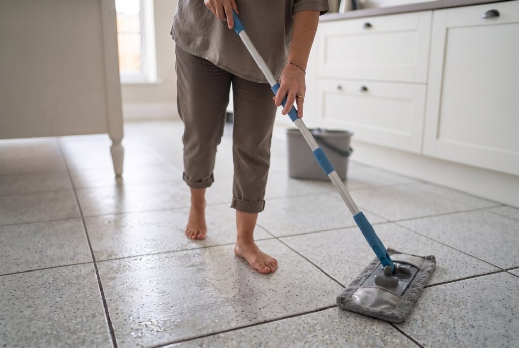 A person using a microfiber mop to clean a gray tiled floor in a kitchen.