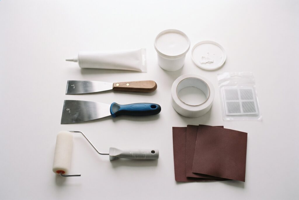 A set of essential drywall repair tools, including spackle, putty knives, mesh patches, and sandpaper.