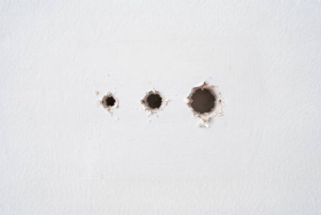A series of three holes in a white wall, ranging from small to large sizes.