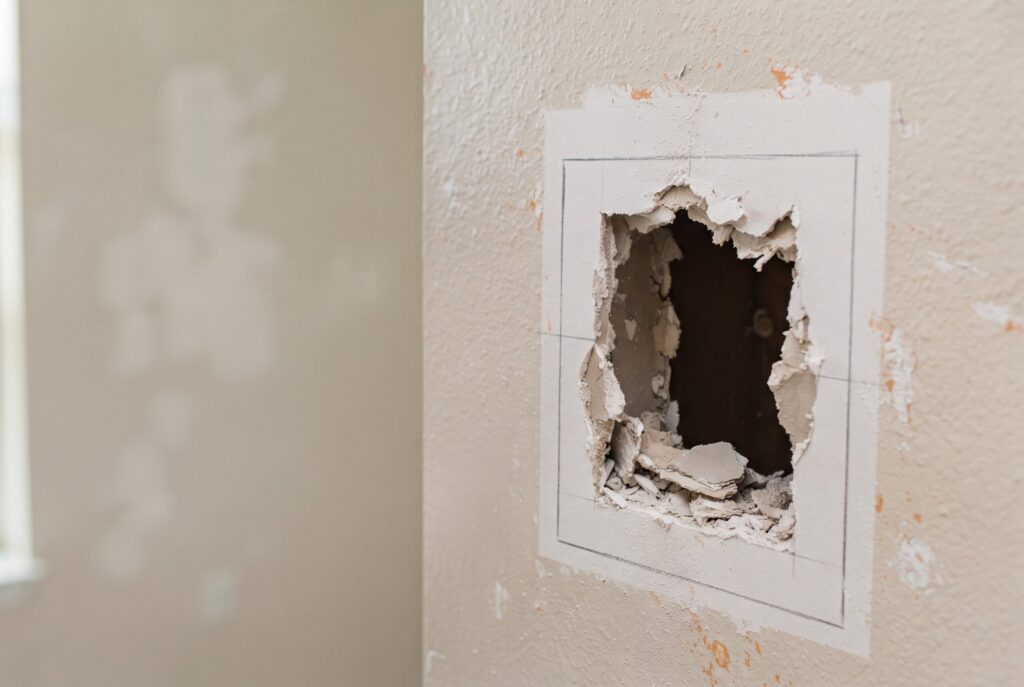 A hole in a drywall section that has been squared off with pencil lines for a clean repair.