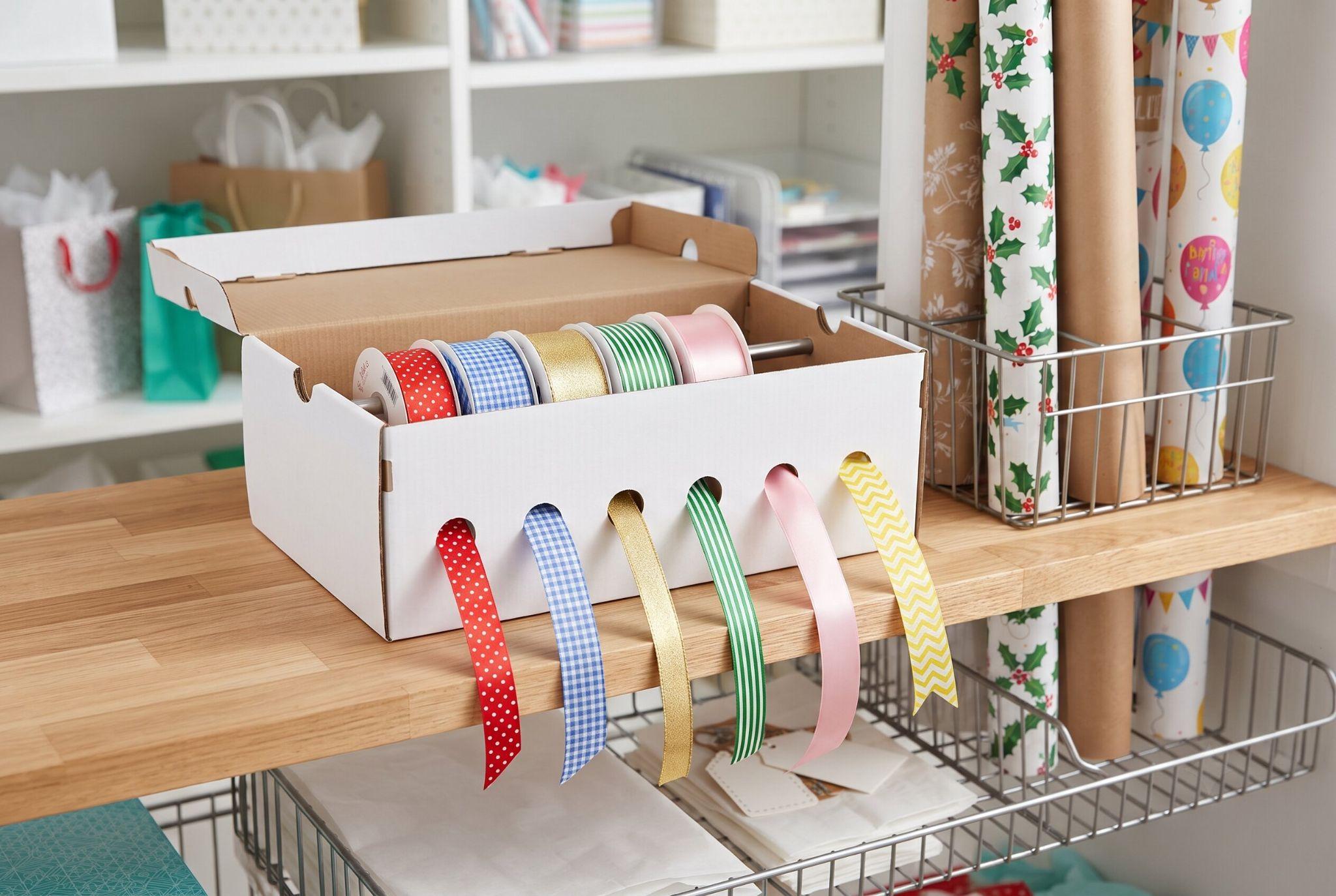 An empty shoebox with holes punched in the side, dispensing ribbon spools from inside.