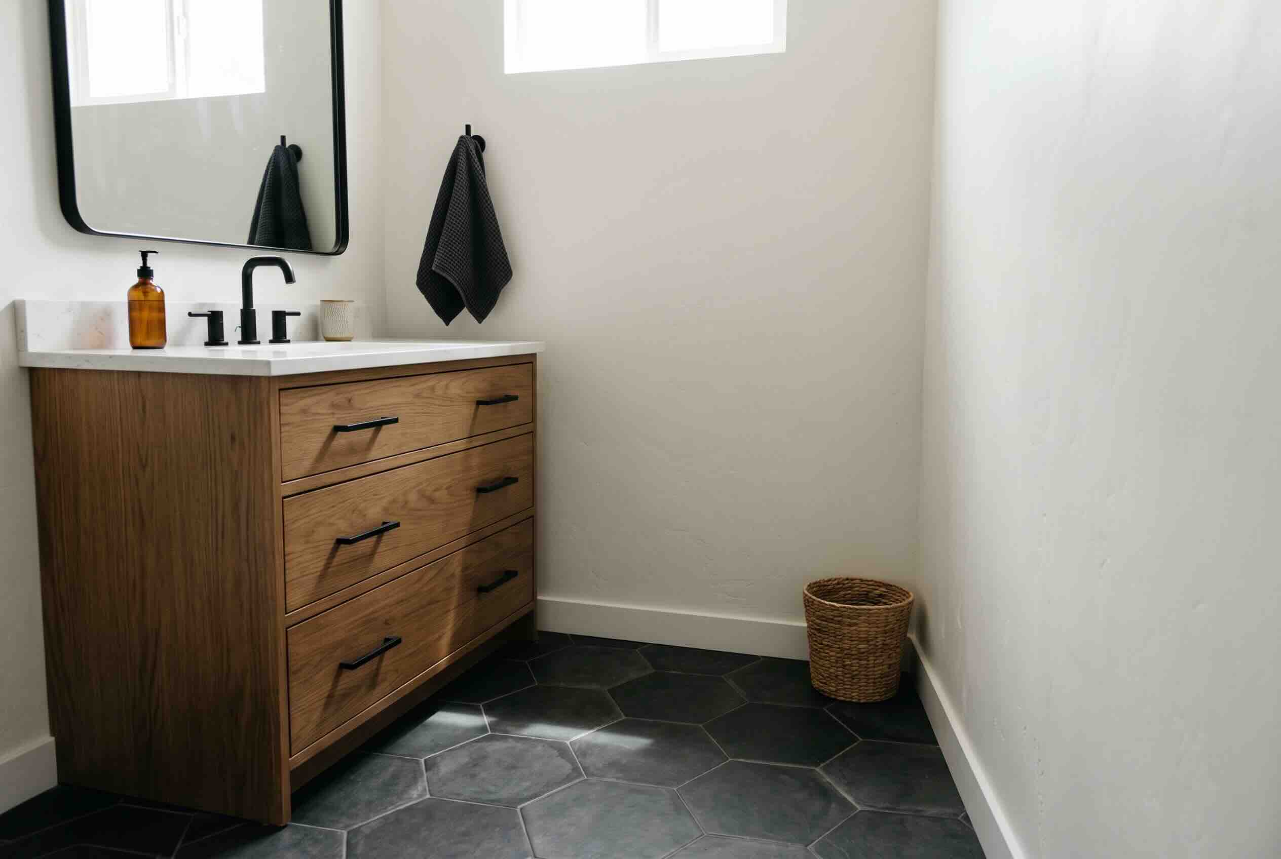 A bathroom floor covered in dark grey hexagonal tiles with a wooden vanity.
