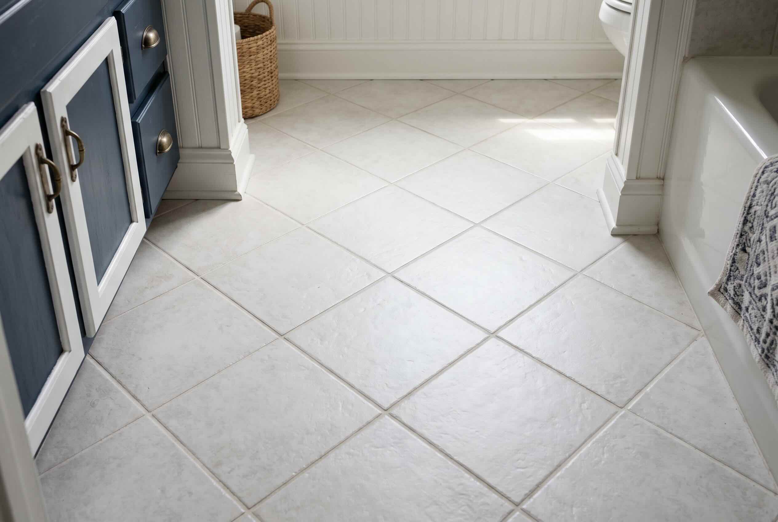 A bathroom floor with large, light-colored square tiles laid in a diagonal pattern.