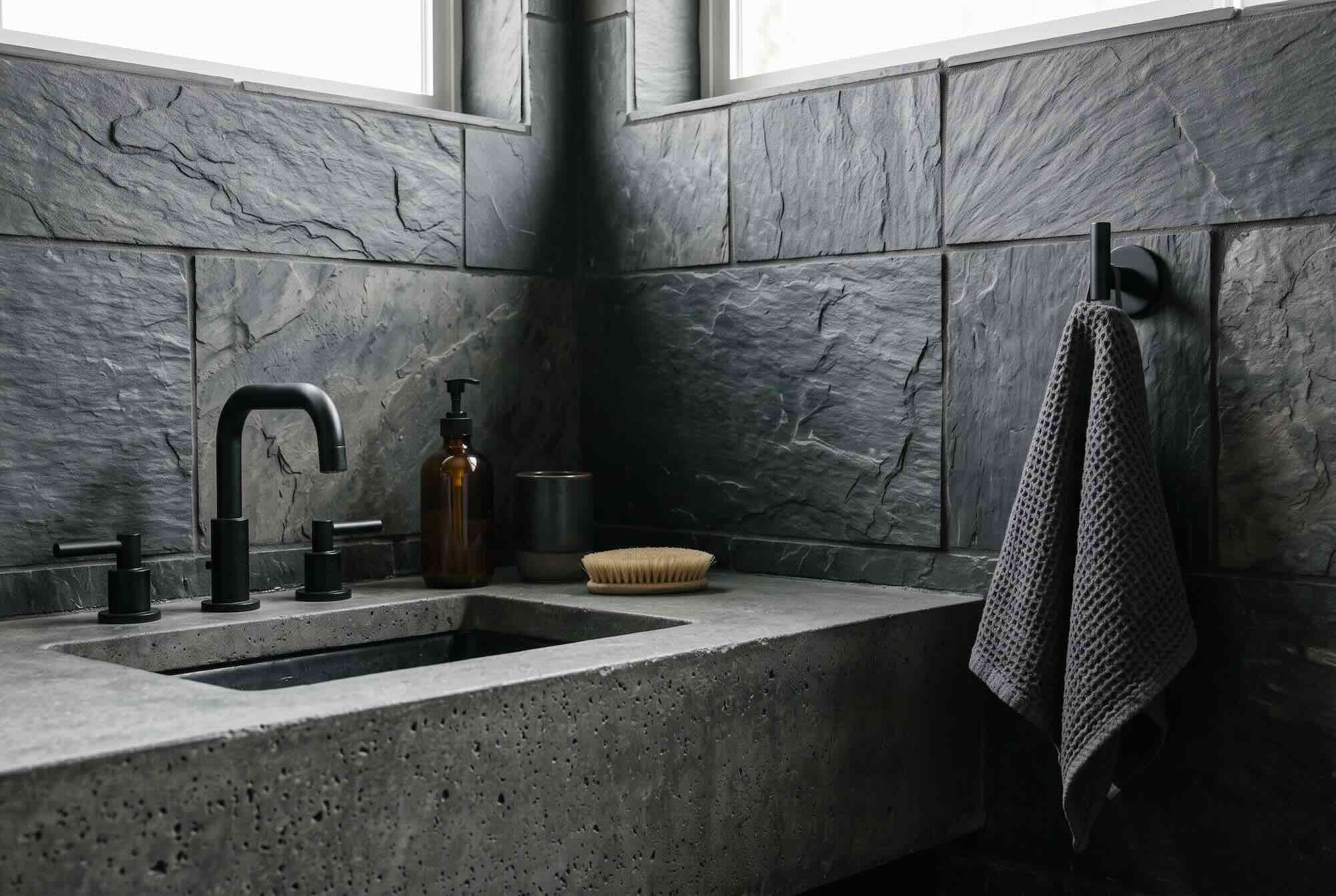 A bathroom sink and wall finished in rugged, dark slate-look tile.