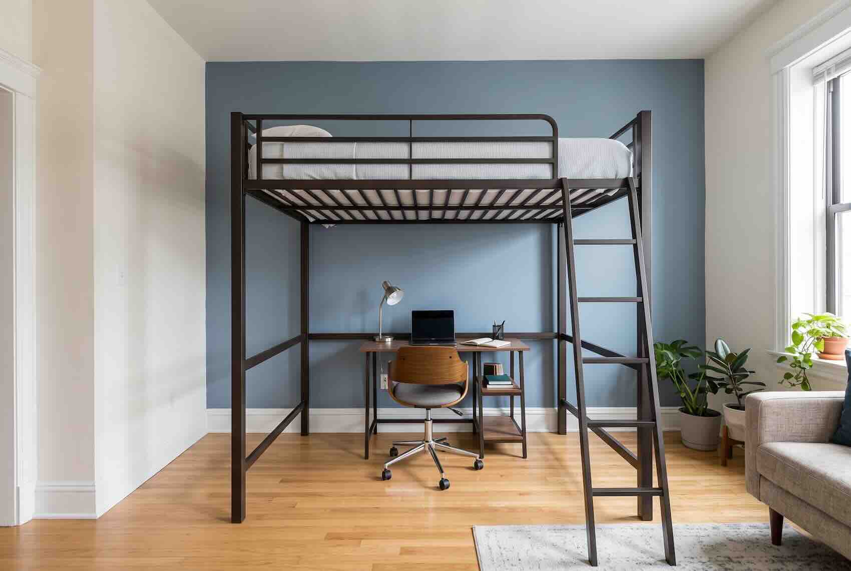 A black metal loft bed with a mattress on top and a desk set up underneath.