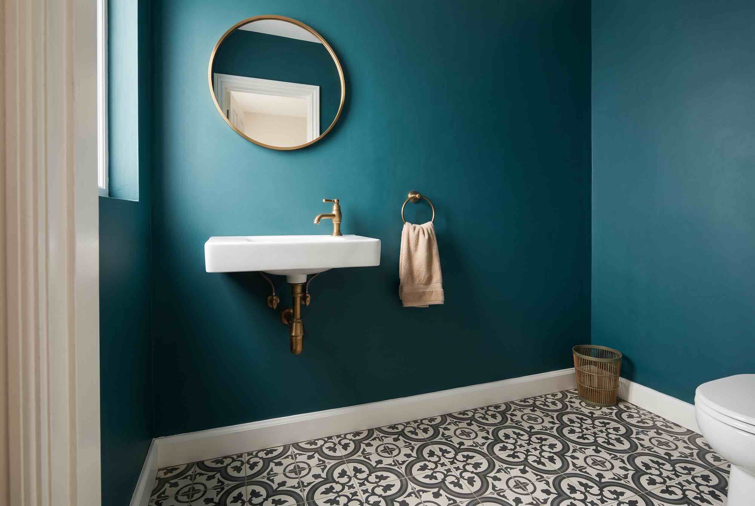 A compact, wall-mounted rectangular sink in a small bathroom with dark teal walls and patterned floor tile.