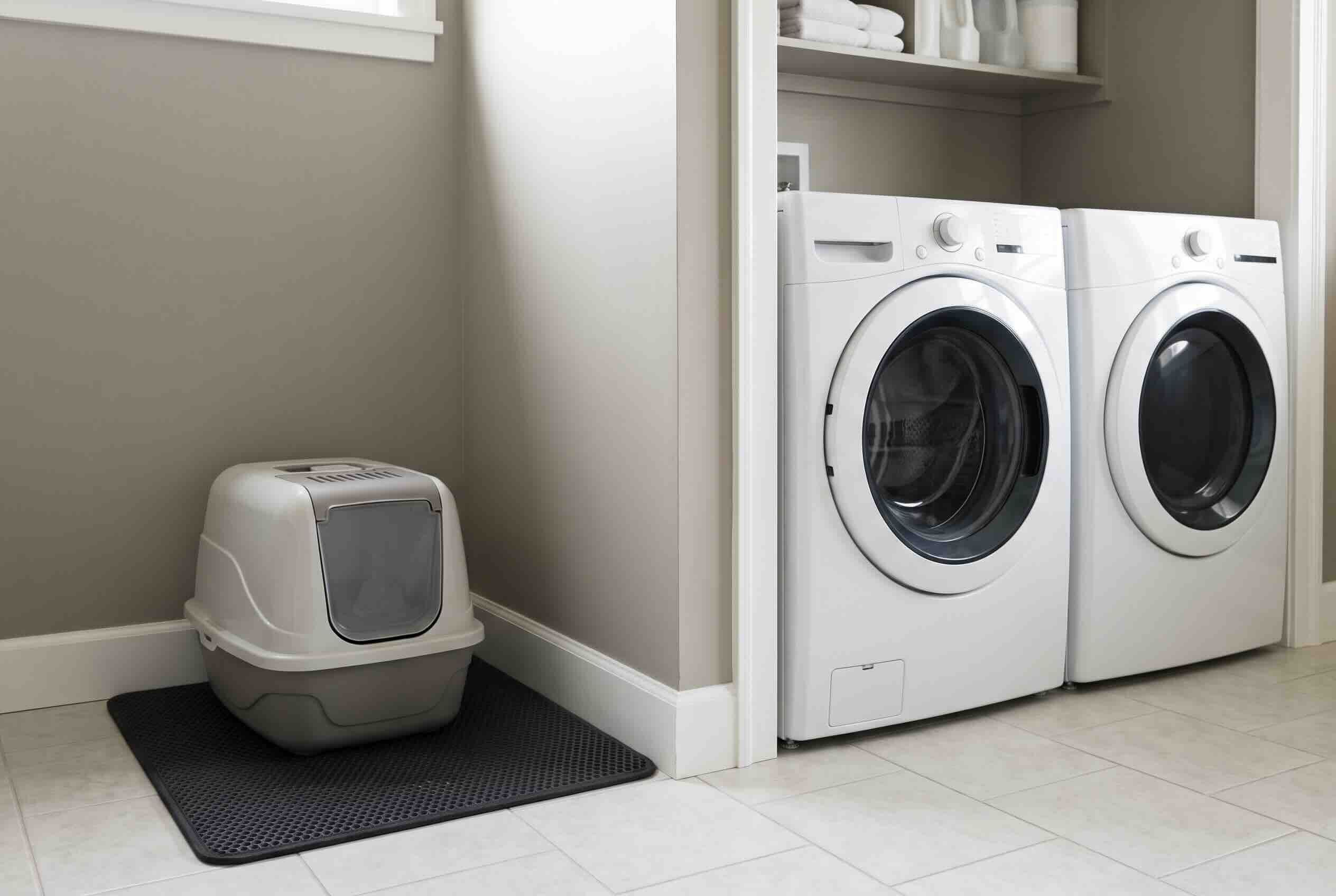 A covered litter box on a black mat placed next to a white washing machine and dryer.