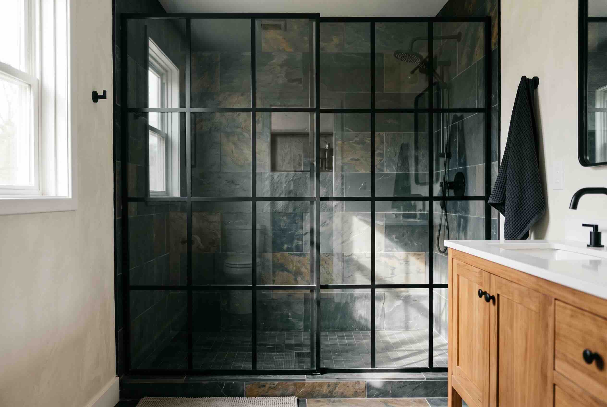 A glass shower enclosure with a black grid frame in a modern bathroom.