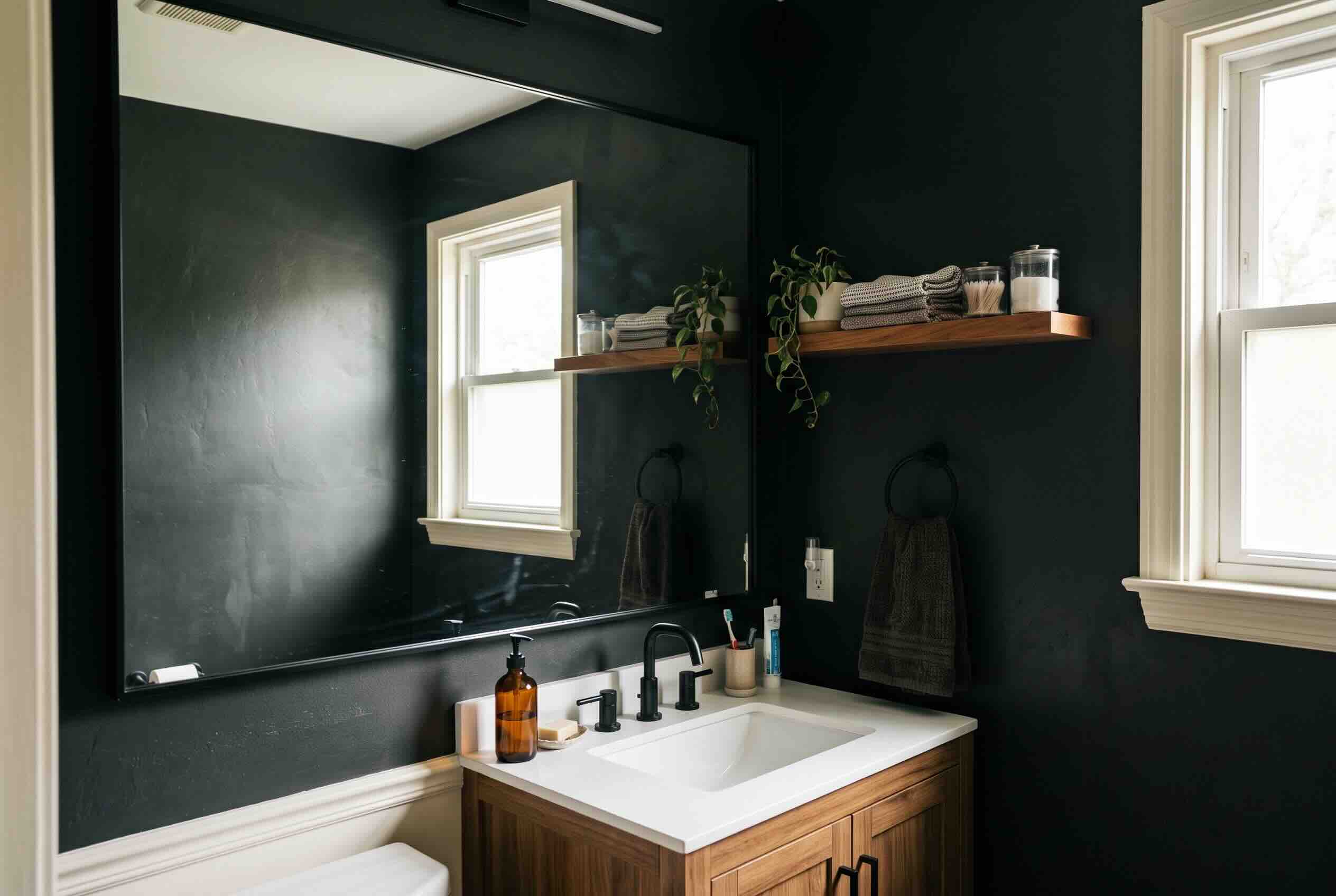 A large, frameless mirror mounted above a vanity on a dark green wall.