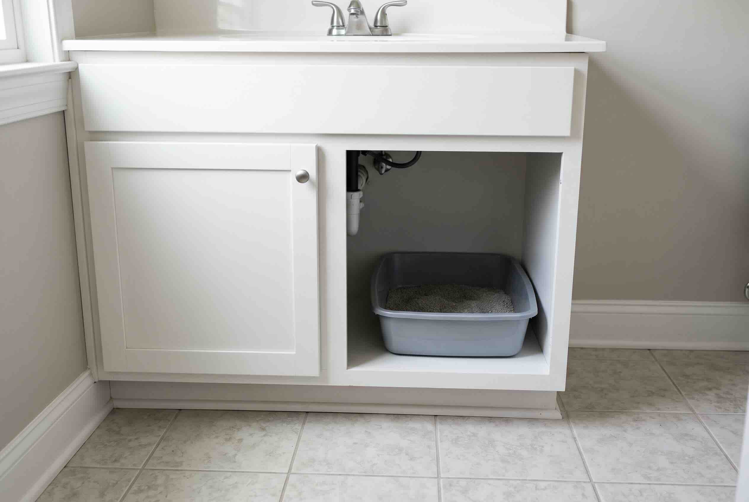 A litter box tucked inside an open under-sink bathroom vanity cabinet.