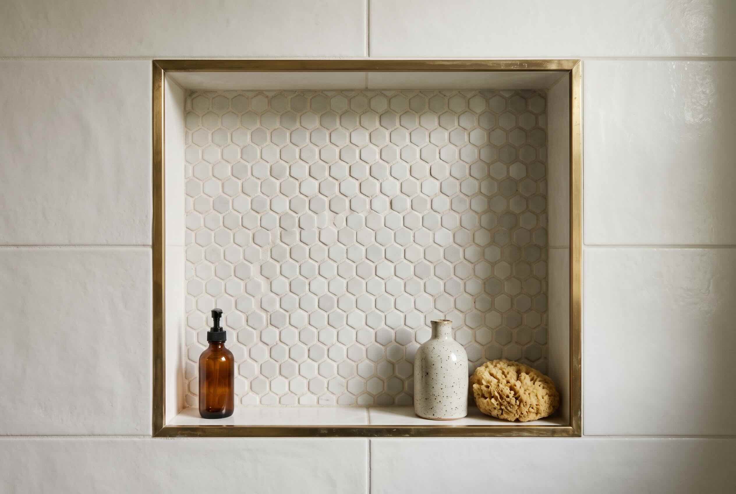 A recessed shower niche lined with small, light-colored hexagonal accent tiles.