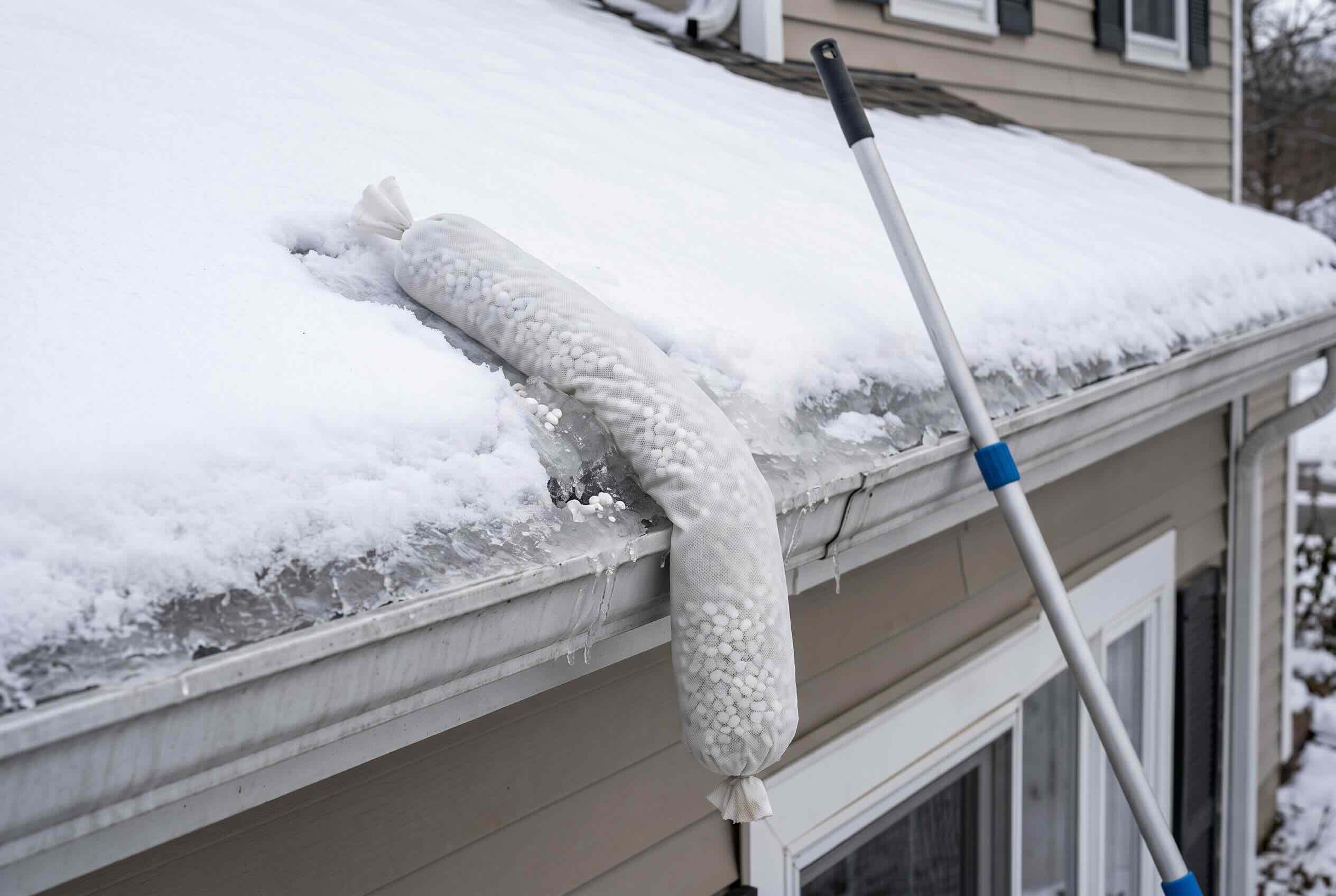 A sock filled with ice melt positioned vertically across a snow-covered gutter.