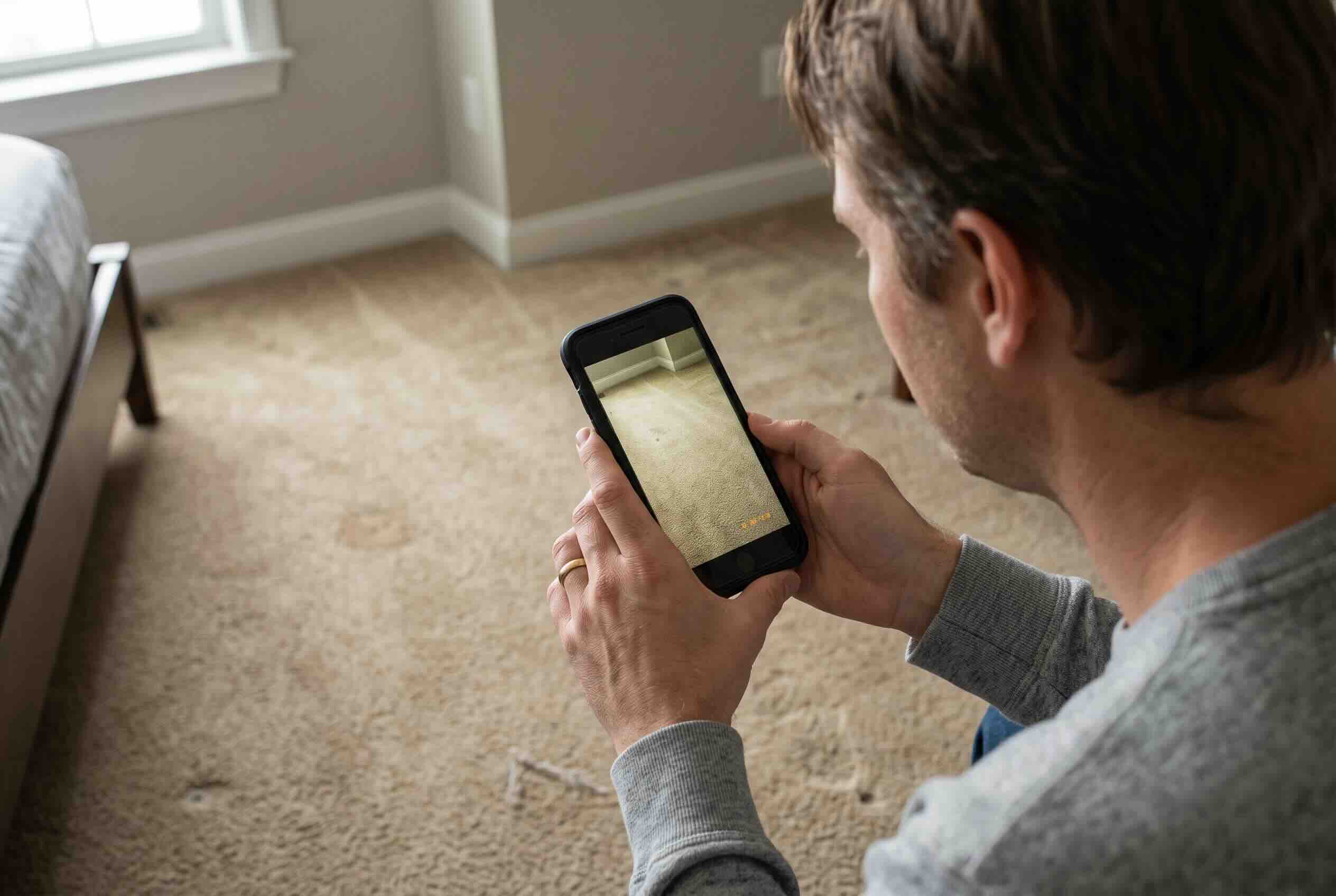 A tenant taking dated photos of the carpet during move-out with a smartphone.
