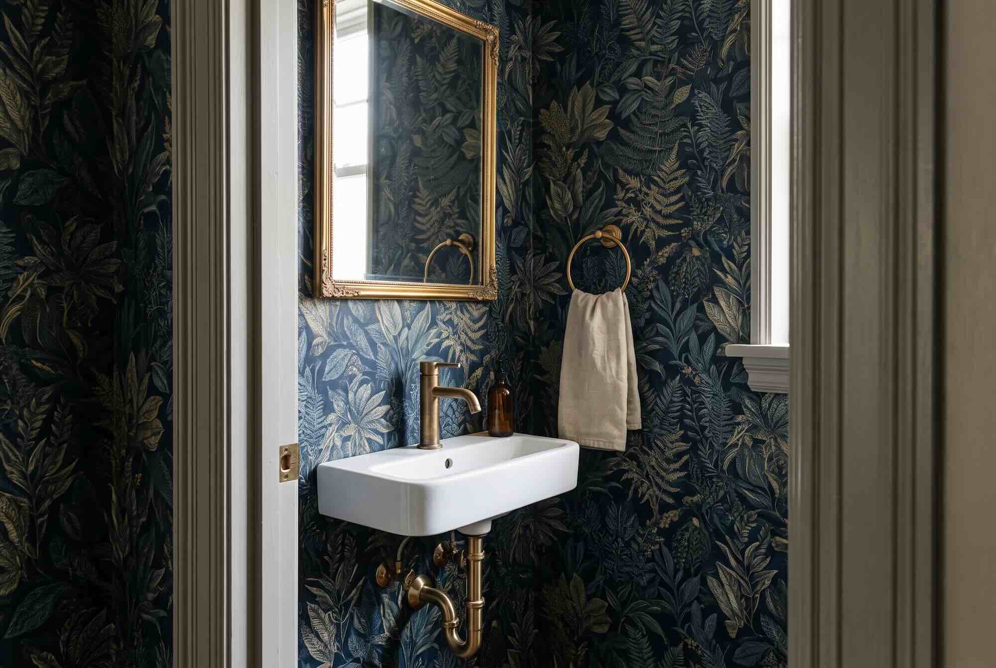 A wall-mounted sink set against bold, dark botanical peel-and-stick wallpaper in a small powder room.