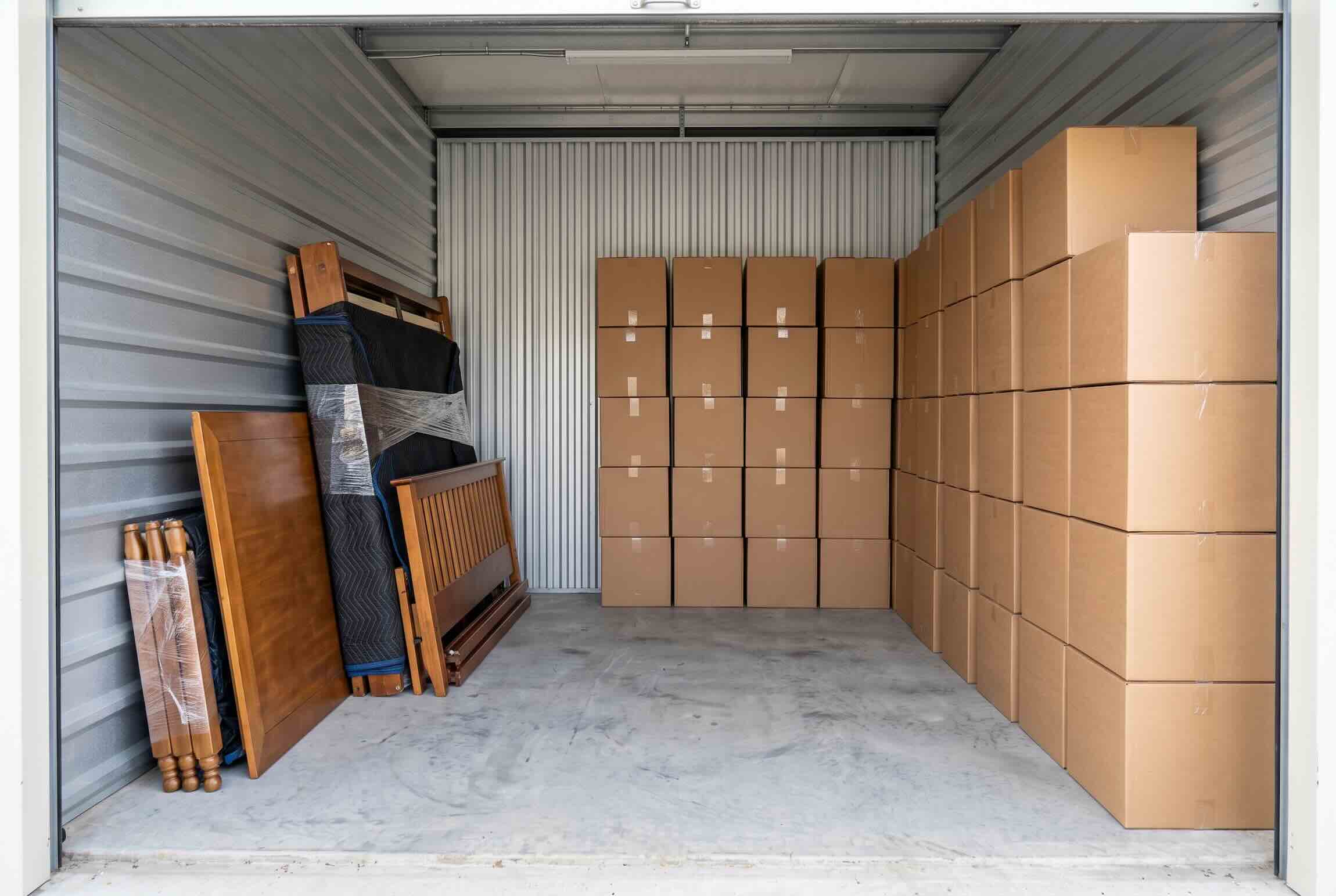 A wrapped mattress, bed frame, and stacked boxes inside a storage unit.