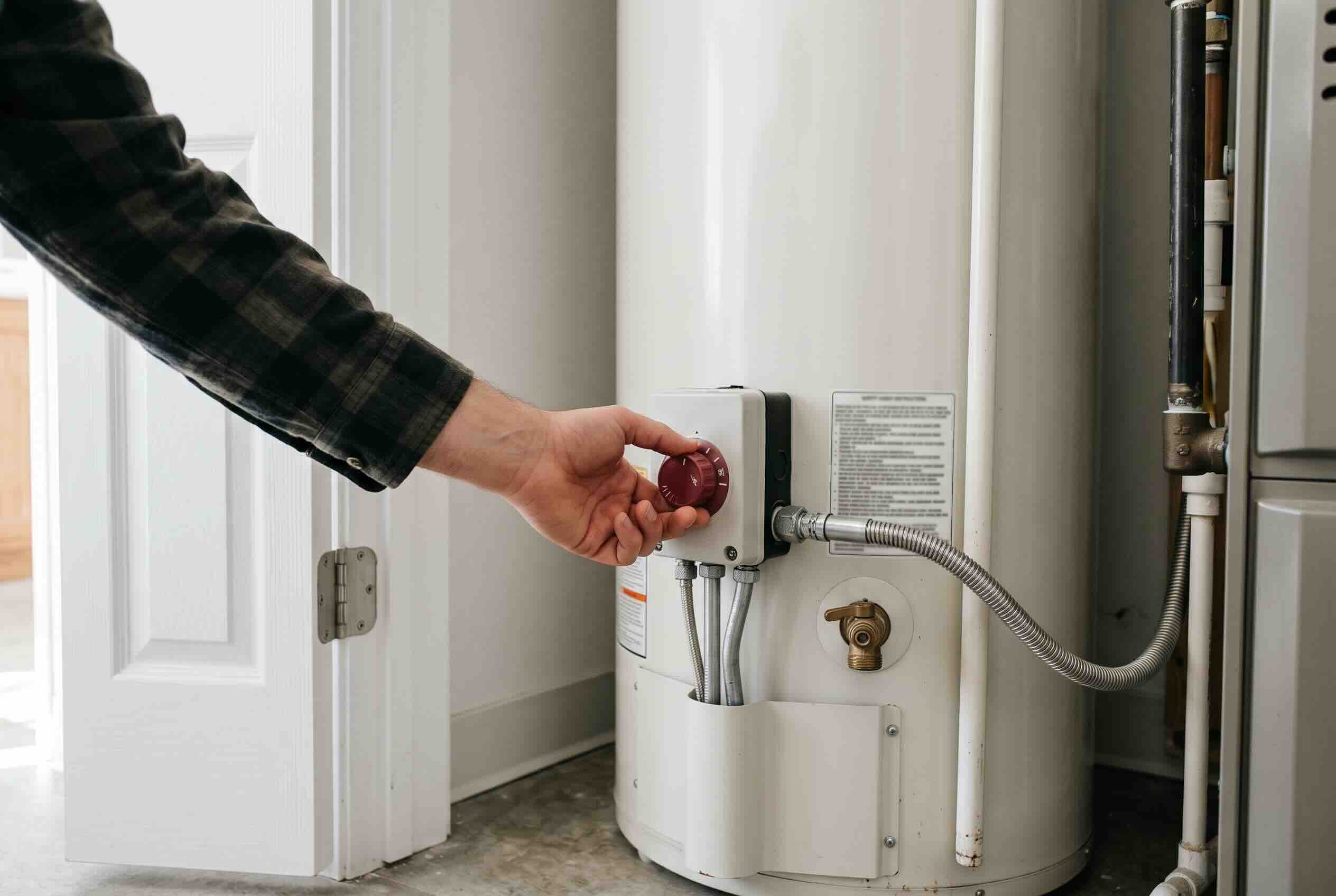 Adjusting the red temperature control dial on a large white residential water heater.