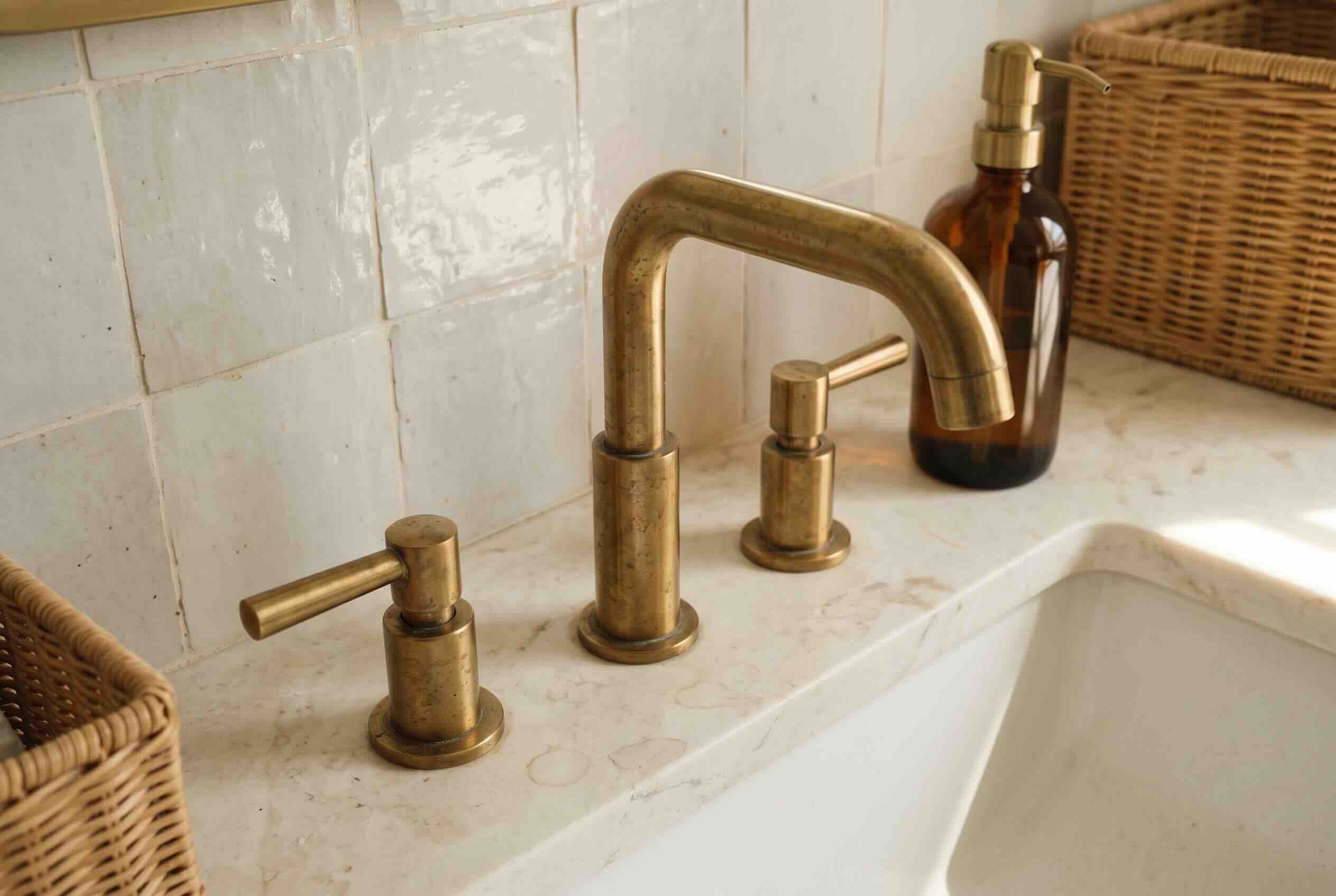 An aged brass faucet on a marble counter against square tiles.