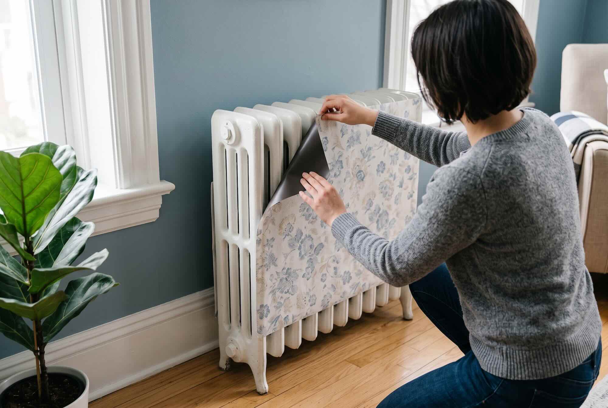 Applying a floral patterned magnetic wrap to the front of a white cast iron radiator.