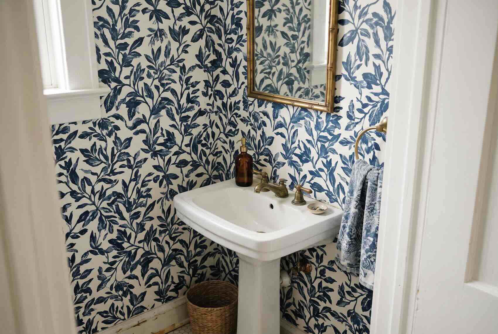 Bold blue-and-white botanical wallpaper behind a classic pedestal sink.