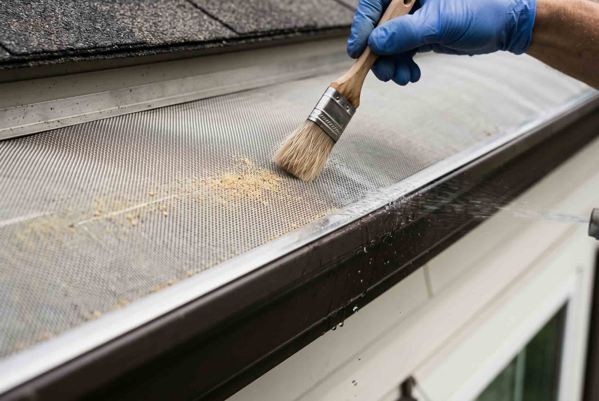 Brushing fine grit and pollen off a micro-mesh gutter guard surface.