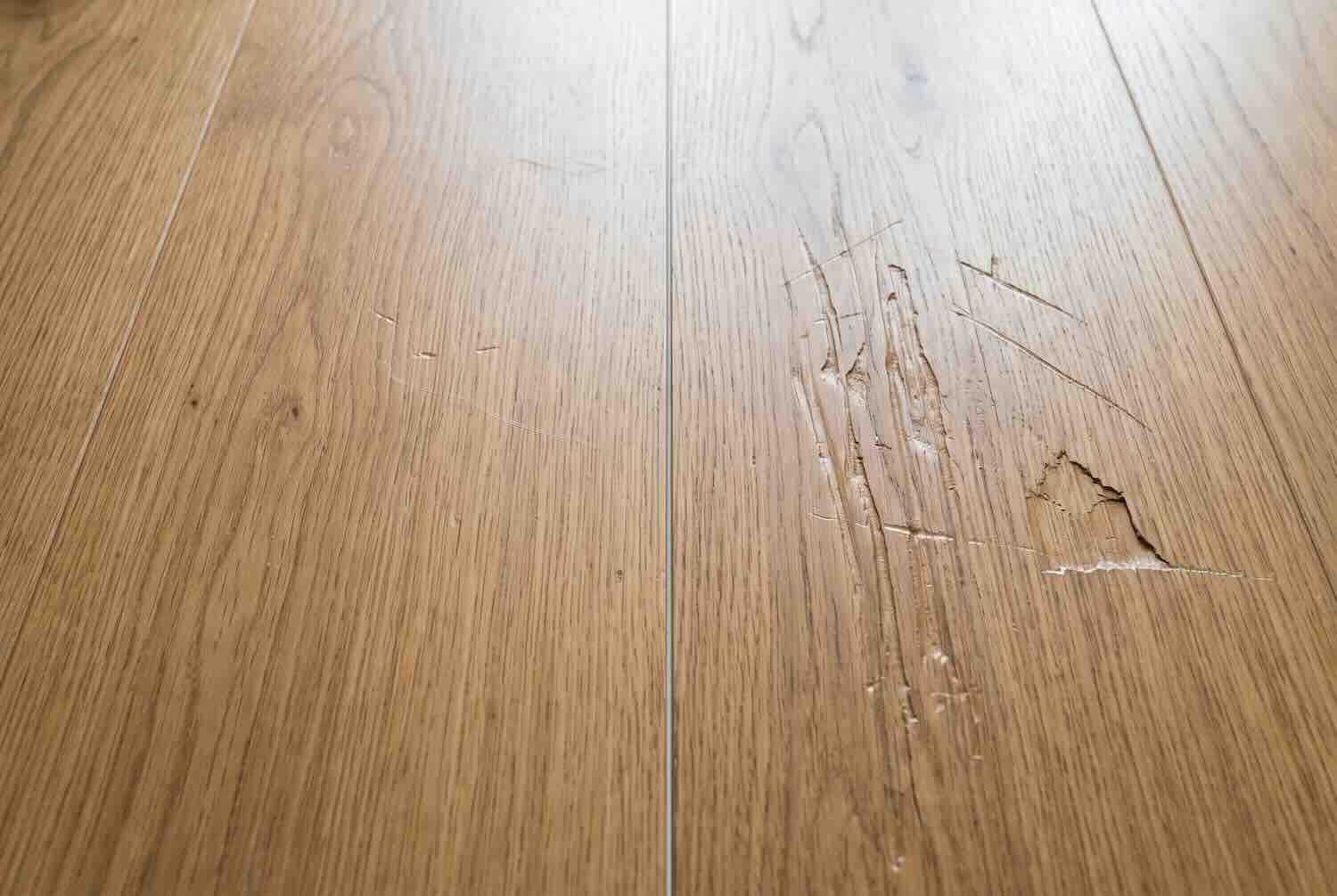 Deep gouges and scratches in a hardwood floor, which are considered tenant damage.