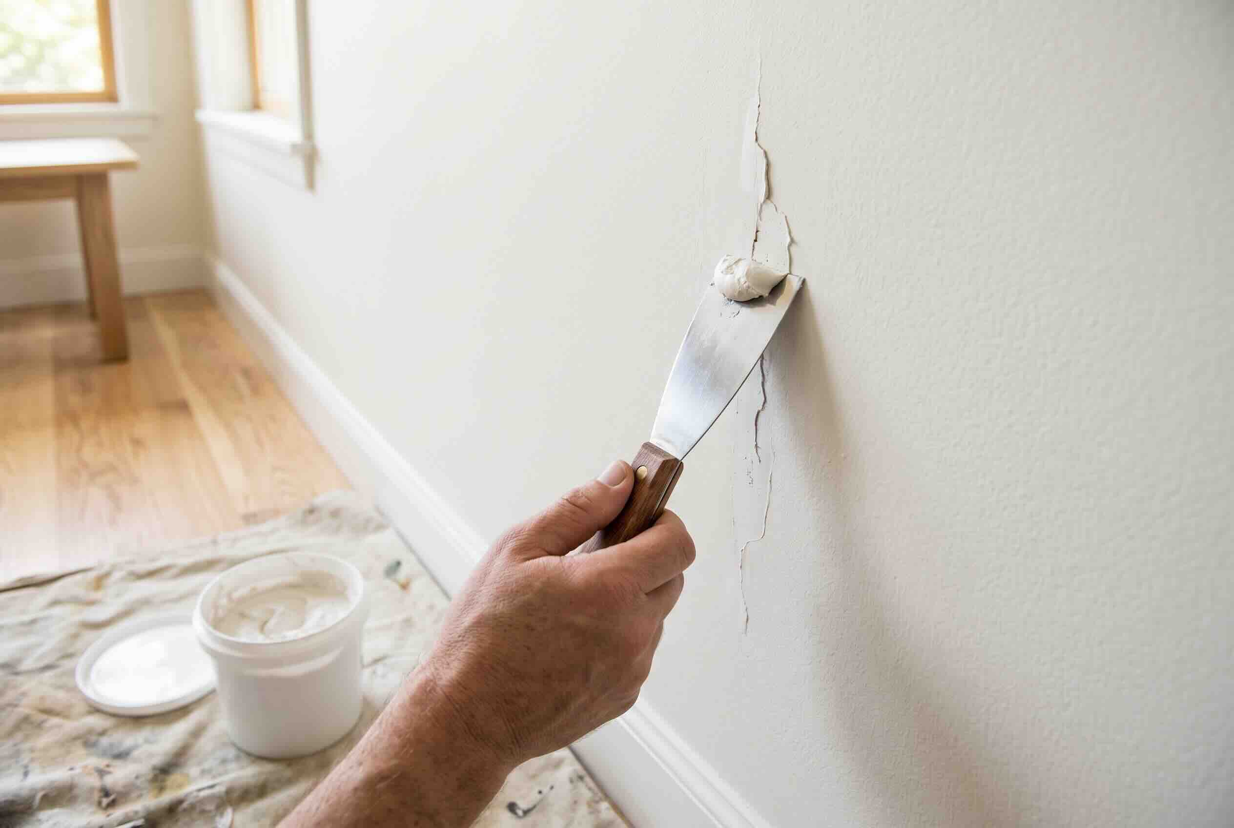 Filling a crack in the wall with spackle using a putty knife.